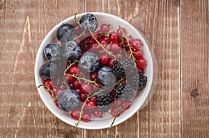 abundance of berries in a white bowl/ abundance of berries in a white bowl on a wooden background. Top view