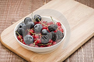 abundance berries in a white bowl/ abundance of berries in a white bowl on a wooden surface