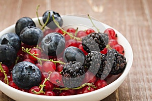 abundance berries in a white bowl / abundance of berries in a white bowl on a wooden surface. Selective focus