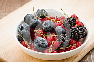 abundance of berries in a white bowl / abundance of berries in a white bowl on a wooden surface. Selective focus