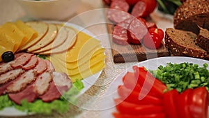 The abundance of food lying on the table. Slices of cucumbers, tomatoes, sausage, ham and meat spread out on plates