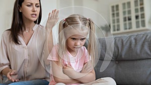 Abused kid girl sitting on couch back to moralizing mother.