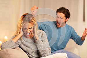 Abusive Husband Shouting At Wife Sitting On Couch At Home