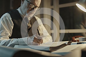 Academic professor writing down notes and reading a book