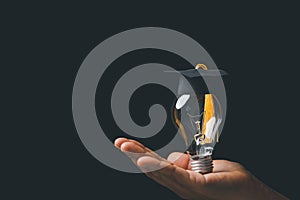 Academy and success graduate education concept. Businessman hand holding bright, electric light bulb with degree cap on black