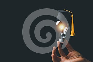 Academy and success graduate education concept. Businessman hand holding bright, electric light bulb with degree cap on black