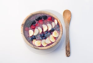 Acai berry smoothie in a wooden bowl topped with bananas, blueberries, raspberries and blackberries