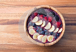 Acai berry smoothie in a wooden bowl topped with bananas, blueberries, raspberries and blackberries