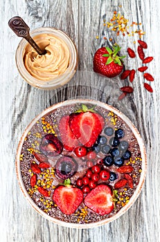 Acai breakfast superfoods smoothies bowl with chia seeds, bee pollen, goji berry toppings and peanut butter. Overhead