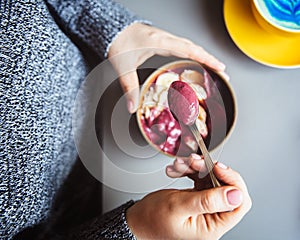 Acai smoothie, granola, seeds, fresh fruits in a wooden bowl in female hands on grey table. Eating healthy breakfast bowl. Top