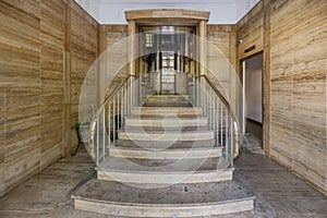 Access portal to the building with brown marble floors on the walls, stairs with golden metal railing and vintage elevator