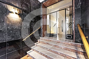 Access portal to a residential building with marble stairs of various shades and polished black walls