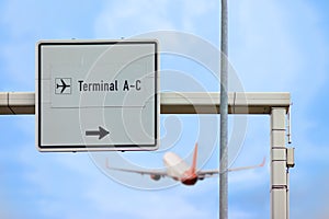 Access to the airport. A large sign reading Terminal A-C. An airplane takes off.