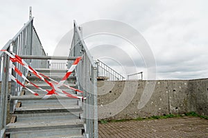 The access to metal staircase is disabled with plastic barrier tape in red and white.