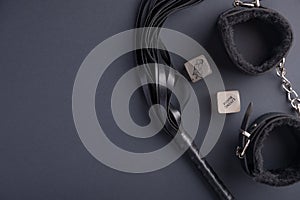 Accessories for bdsm on a black background. Leather lash and leather handcuffs and sex cubes. Valentine`s Day. Erotic shop. Copy