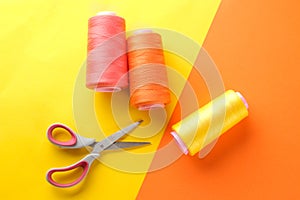 Accessories for sewing and needlework. Scissors and spools of thread on a bright yellow and orange background