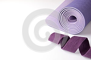 Accessories for yoga, pilates or fitness. Purple yoga mat and purple belt on a white background with copyspace