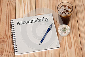 Accountability concept on notebook, pen cactus and coffee cup on wooden table. Business concept