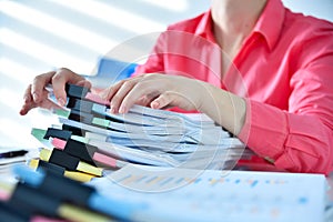 Accountant or businesswoman searching in stack of documents for business report