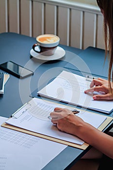 An accountant is examining a large amount of income and expense documents laying on their desks in their offices to summarize