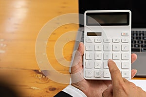 The accountant presses the calculator to calculate the income and in the payout, there is a laptop on the table.