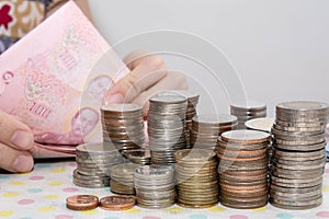 Accounting concepts present by Female hand counting baht bills behind money coin stacks isolated on white