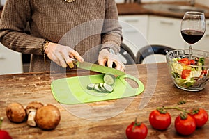 Accurate good-looking lady in beige sweater chopping cucumber