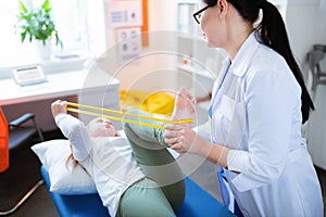 Accurate long-haired doctor bending skinny leg of little girl