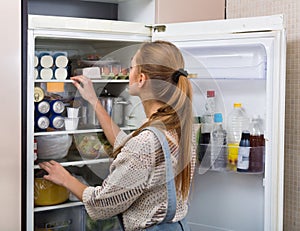 Accurate and positive girl standing near fridge