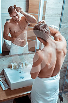 Accurate tidy guy staying in front of the mirror in a white towel
