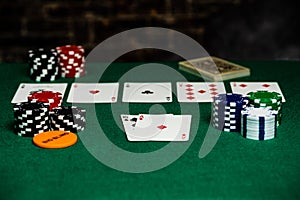 4 aces in Texas Hold-em on a green felt playing surface surrounded by betting chips and a big blind chip.  Bright foreground with