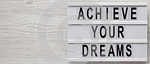 `Achieve your dreams` words on a lightbox on a white wooden background, top view. Overhead, from above, flat lay. Copy space