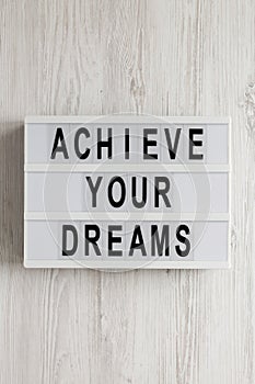 `Achieve your dreams` words on a modern board on a white wooden background, top view. Overhead, from above, flat lay. Close-up