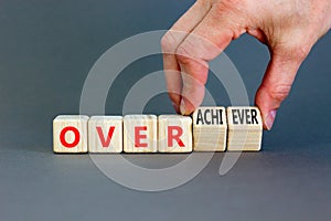 Achiever or overachiever symbol. Businessman turns wooden cubes and changes word Achiever to Overachiever. Beautiful grey table