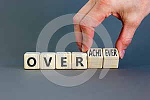 Achiever or overachiever symbol. Businessman turns wooden cubes and changes word Achiever to Overachiever. Beautiful grey table