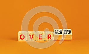 Achiever or overachiever symbol. Businessman turns wooden cubes and changes word Achiever to Overachiever. Beautiful orange