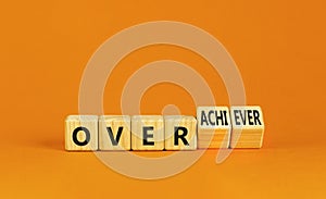 Achiever or overachiever symbol. Businessman turns wooden cubes and changes word Achiever to Overachiever. Beautiful orange