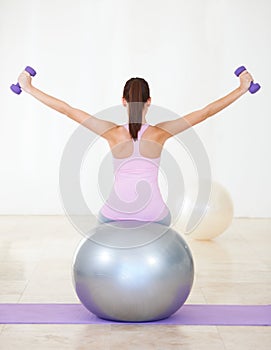 Achieving her fitness objectives. Rearview shot of a young woman sitting on an exercise ball and doing some