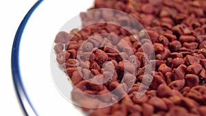 Achiote seeds. Annatto grains in white plate. Red natural culinary dye for cooking.