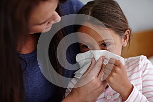 Achoo. a mother helping her sick daughter to blow her nose.