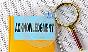 ACKNOWLEDGMENT text on sticker on notebook with magnifier and chart. Business concept