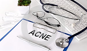 ACNE text on white paper on white background. stethoscope ,glasses and keyboard
