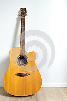 An acoustic dreadnought guitar leaned against the white wall background. Veritcal image copy space