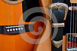 Acoustic and electric guitars and leather strap with silver buckle close-up.