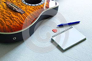 Acoustic guitar on bed next to notebook and pen to compose songs