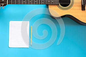 Acoustic guitar and blank paper on blue background, top view.