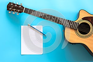 Acoustic guitar and blank paper on blue background, top view.