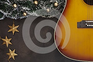 Acoustic guitar and Christmas garland decor with golden Christmas stars on dark brown background