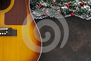 Acoustic guitar and Christmas garland decor with red dekorative balls on dark brown background