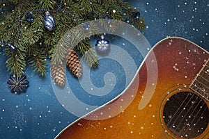 Acoustic guitar and Christmas tree branches with blue dekorative balls on blue background with glitter